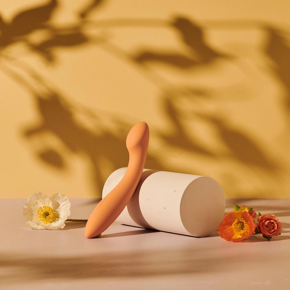 Peach Goodful x Pipedream wand vibrator leaning on a stone cylinder with poppies and a rose, foliage shadows behind, photographed for BuzzFeed by Taylor Miller.