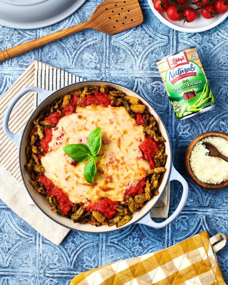 Cheesy green bean casserole topped with tomato sauce and basil in a skillet beside a Libby's Naturals can, for Libby's and BuzzFeed by Taylor Miller.