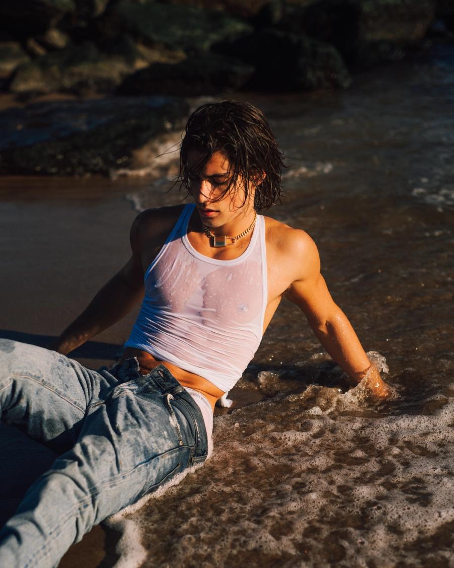 Model Corrado Martini, wearing a white tank and jeans on the beach, photographed for L'Officiel Hommes Poland shot by photographer Taylor Miller.