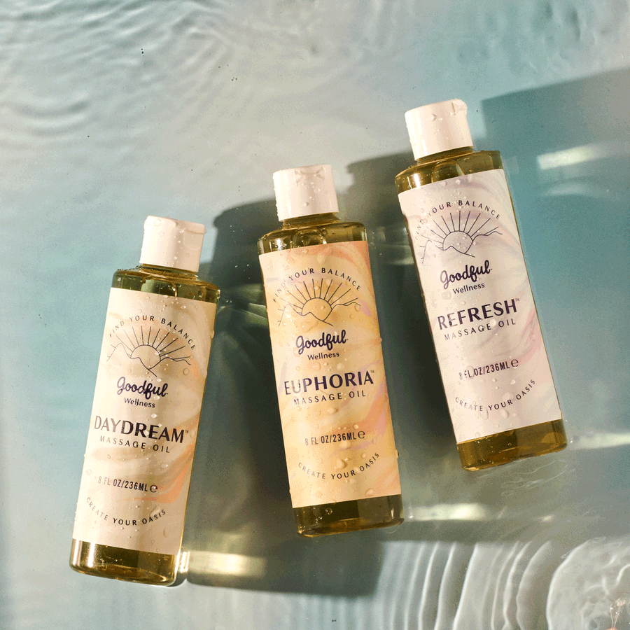 Three Daydream, Euphoria and Refresh body oil bottles drifting on a rippling shallow water surface, photographed by Taylor Miller.