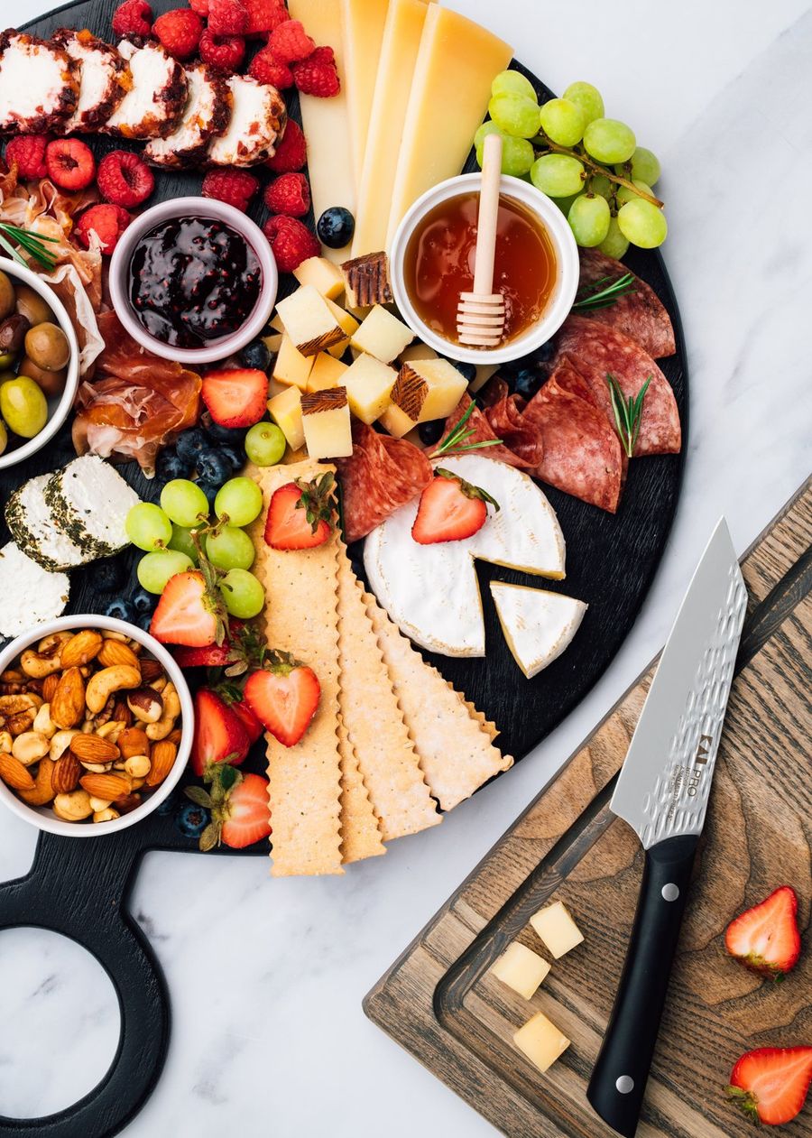 Loaded charcuterie board of cheeses, cured meats, grapes, and berries beside a Kai knife and cubed cheese, photographed for BuzzFeed by Taylor Miller.