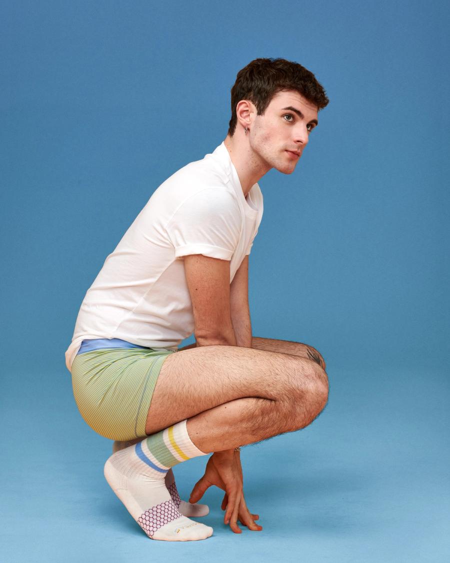 Luca La Via crouches in a white tee, striped boxer briefs, and rainbow-striped Bombas ankle socks, photographed for Bombas Pride 2024 by Taylor Miller.