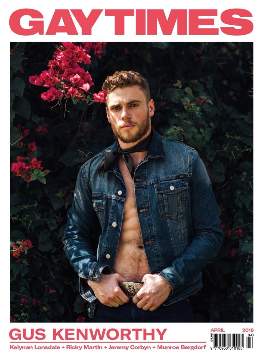 Gus Kenworthy in an open denim jacket and neck scarf against pink bougainvillea on the cover of Gay Times, photographed by Taylor Miller.