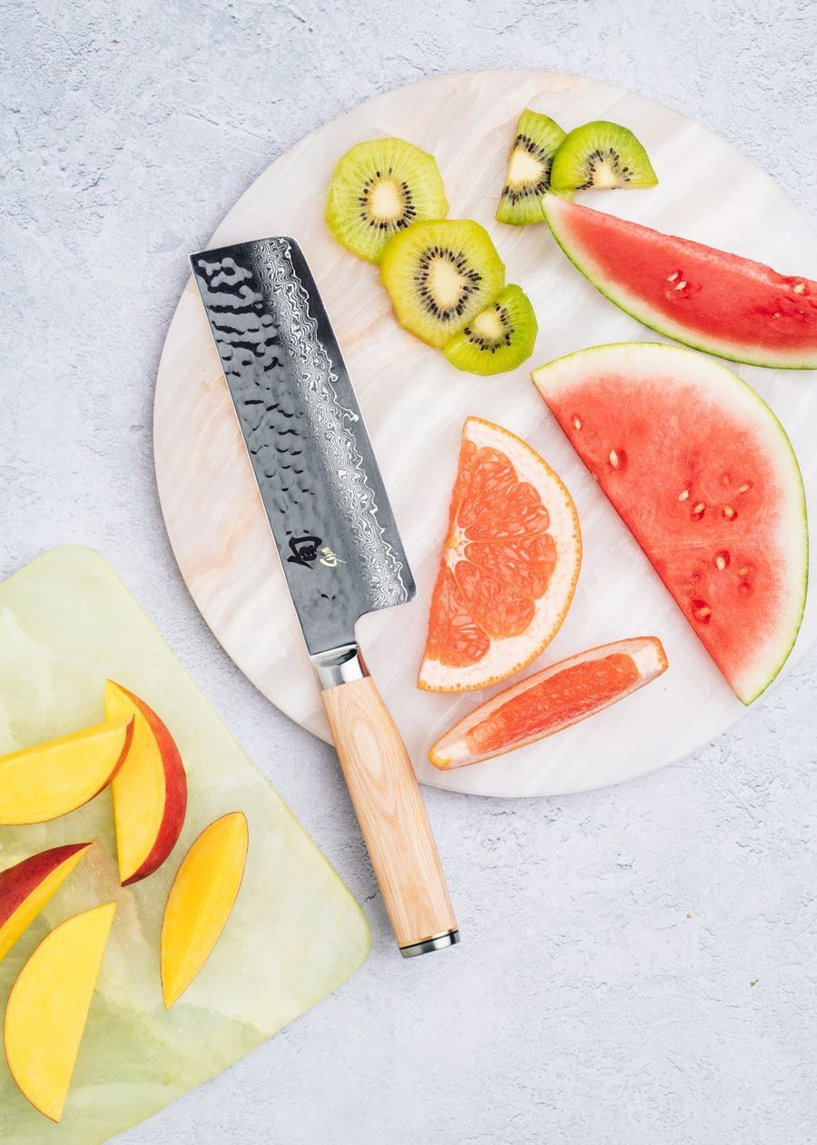 Hammered Kai damascus nakiri knife with a light wood handle amid sliced kiwi, watermelon, grapefruit, and mango, photographed for BuzzFeed by Taylor Miller.