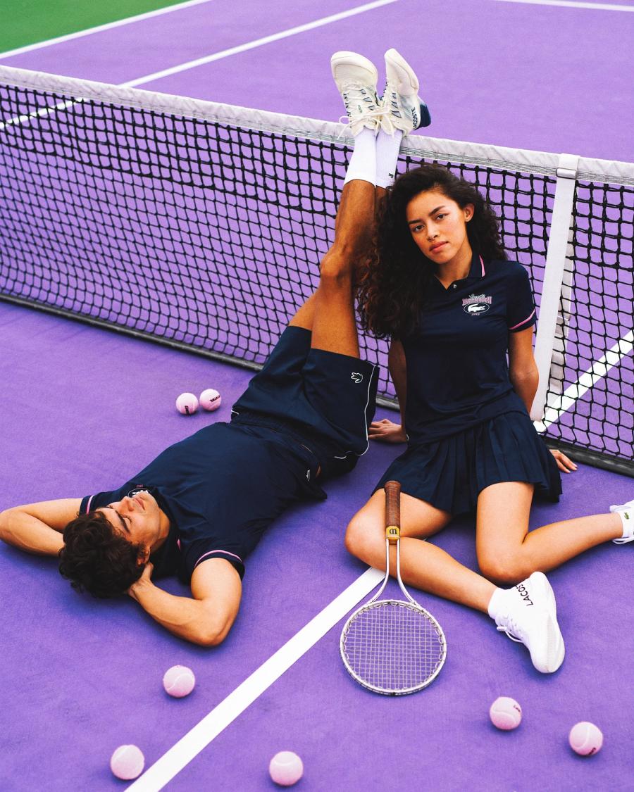 Iago Botelho and Britney Nguyen in navy Lacoste tennis looks rest by the net on a purple court, for Lacoste Miami Open 2025 by Taylor Miller.
