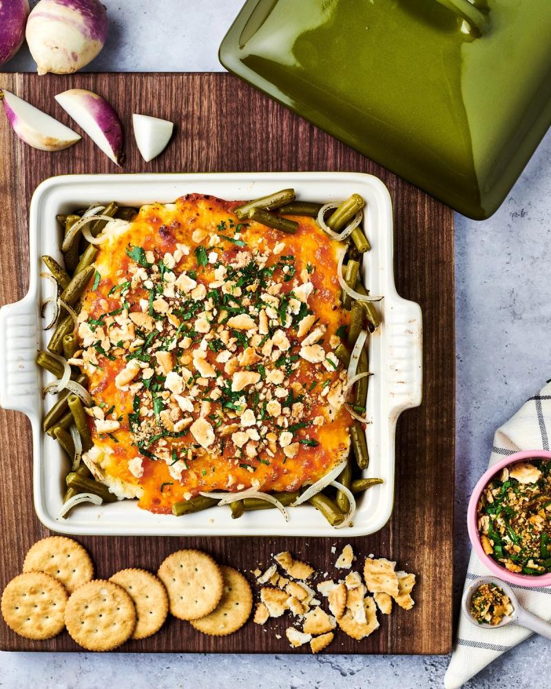 Cheesy green bean dip topped with crushed nuts and herbs, served with crackers on a wood board, for Libby's and BuzzFeed by Taylor Miller.