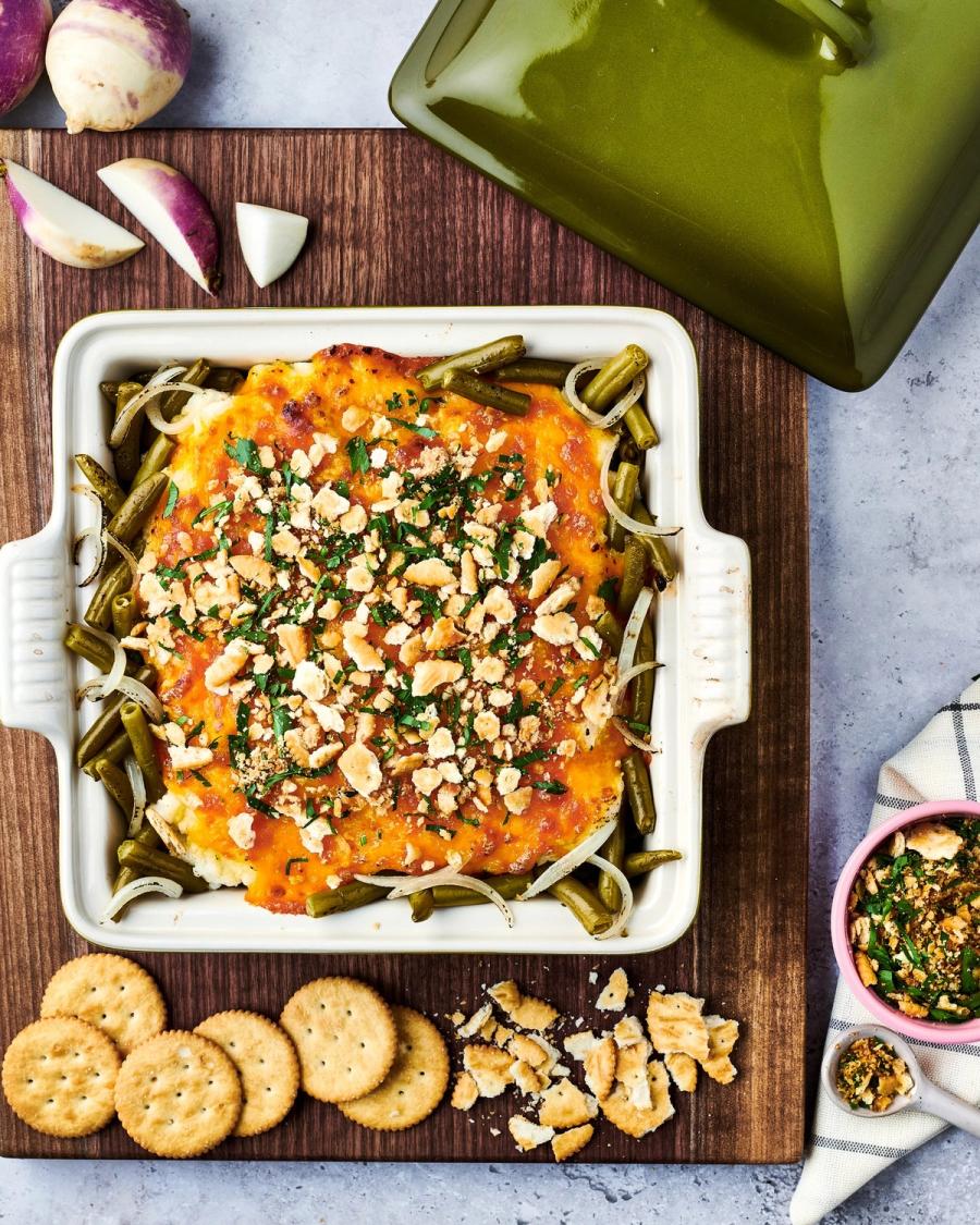 Cheesy green bean dip topped with crushed nuts and herbs, served with crackers on a wood board, for Libby's and BuzzFeed by Taylor Miller.