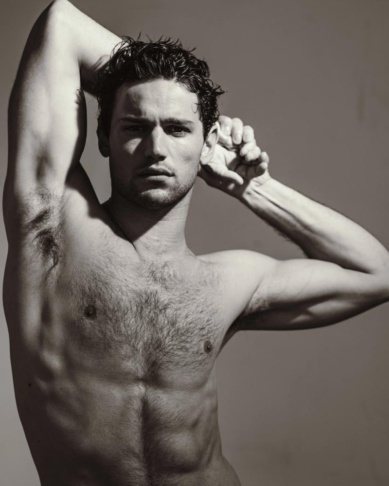 Giacomo Cavalli with wet curly hair posing with one arm raised, in a black and white studio portrait, photographed by Taylor Miller.