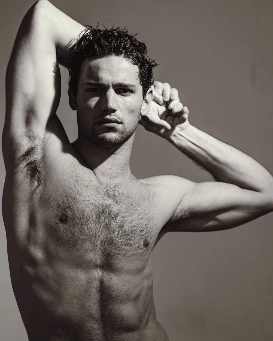 Giacomo Cavalli with wet curly hair posing with one arm raised, in a black and white studio portrait, photographed by Taylor Miller.