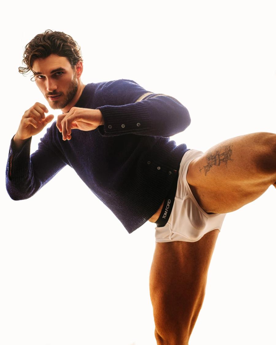 Michael Yerger in a navy knit sweater and white Tom Ford briefs, leg raised in a dynamic pose for L'Officiel Hommes by photographer Taylor Miller.