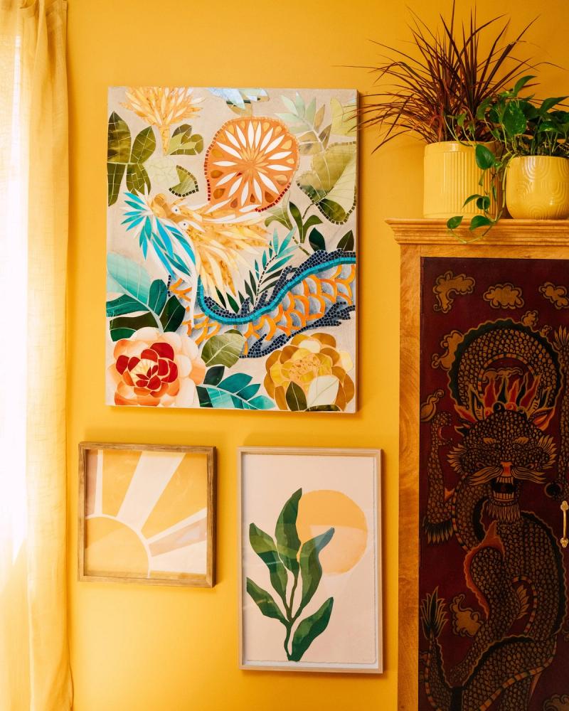 Yellow wall gallery of botanical HomeGoods art with potted plants and a carved cabinet, styled for BuzzFeed by photographer Taylor Miller.