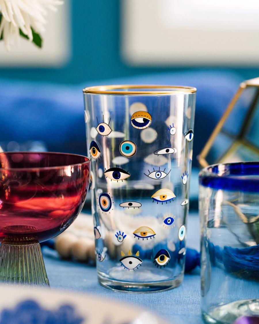 Close-up of a HomeGoods evil-eye glass tumbler among blue and red glassware on a blue table, styled for BuzzFeed by photographer Taylor Miller.