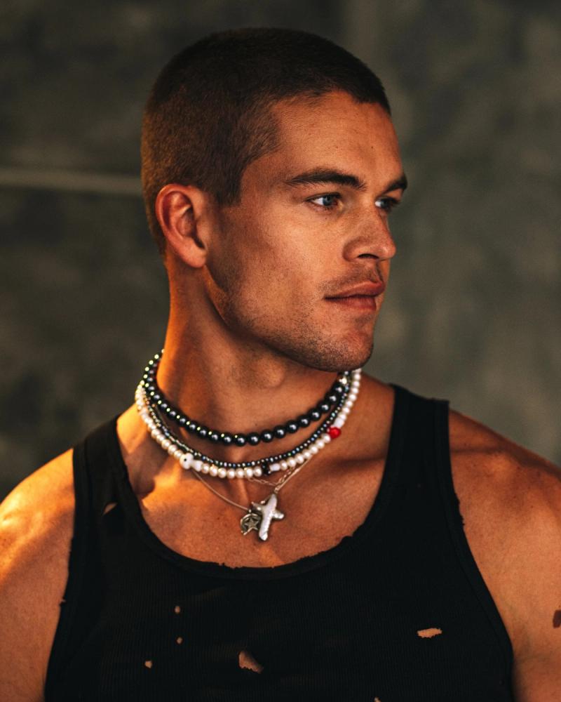 Profile portrait of Mitchell Slaggert in a black distressed tank with layered pearl necklaces and a cross pendant, for Numéro Netherlands by Taylor Miller.