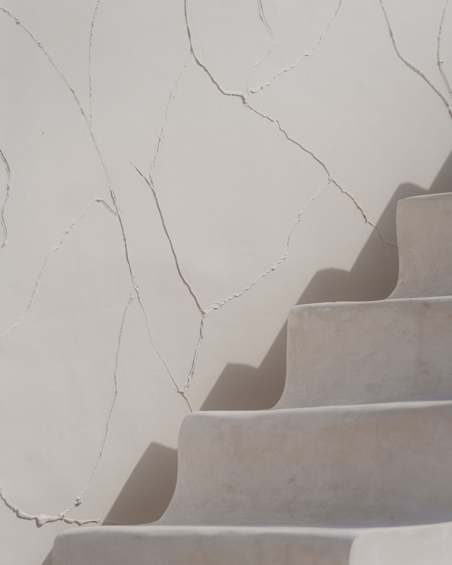 Sunlit sculptural staircase set against textured white wall, minimalist villa architecture and branding detail at House of Creations Bali