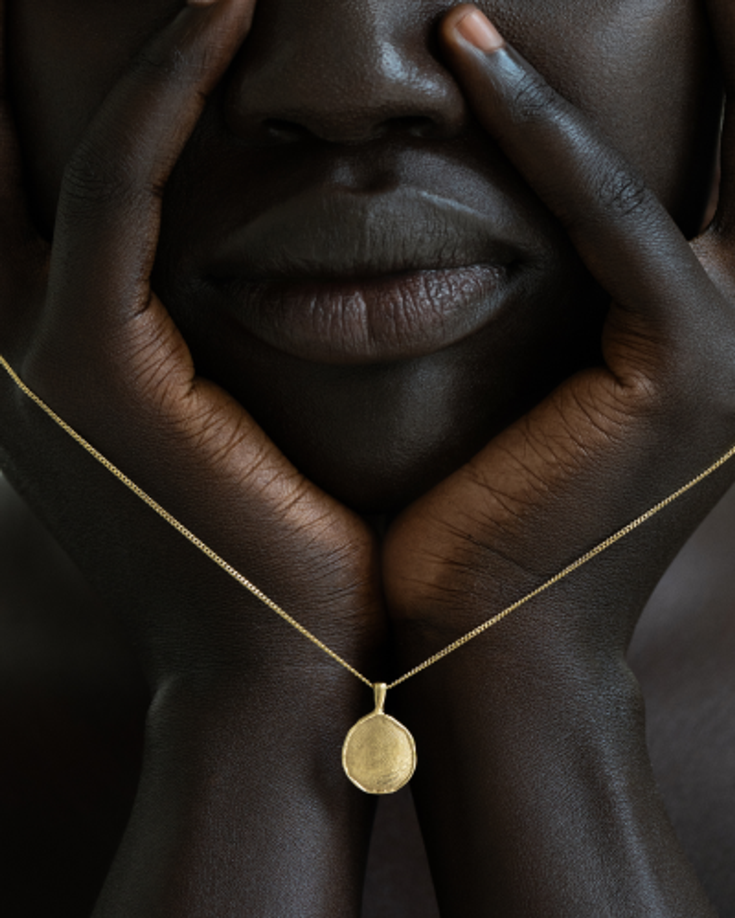 Close‑up of model’s face framed by hands wearing OMOI Jewelry gold Forever Pendant on fine chain, created for Shopify branding and website design by Eeze Studio