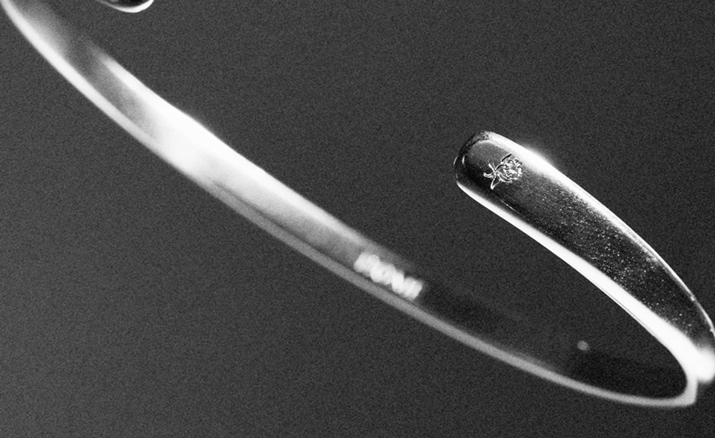 BØME Studios classic silver cuff detail by Eeze Studio Close-up black and white photograph of a slim BØME Studios silver cuff bracelet with a subtle flower hallmark at the end, emphasizing minimal mens jewelry craftsmanship and product branding photography developed by Eeze Studio.