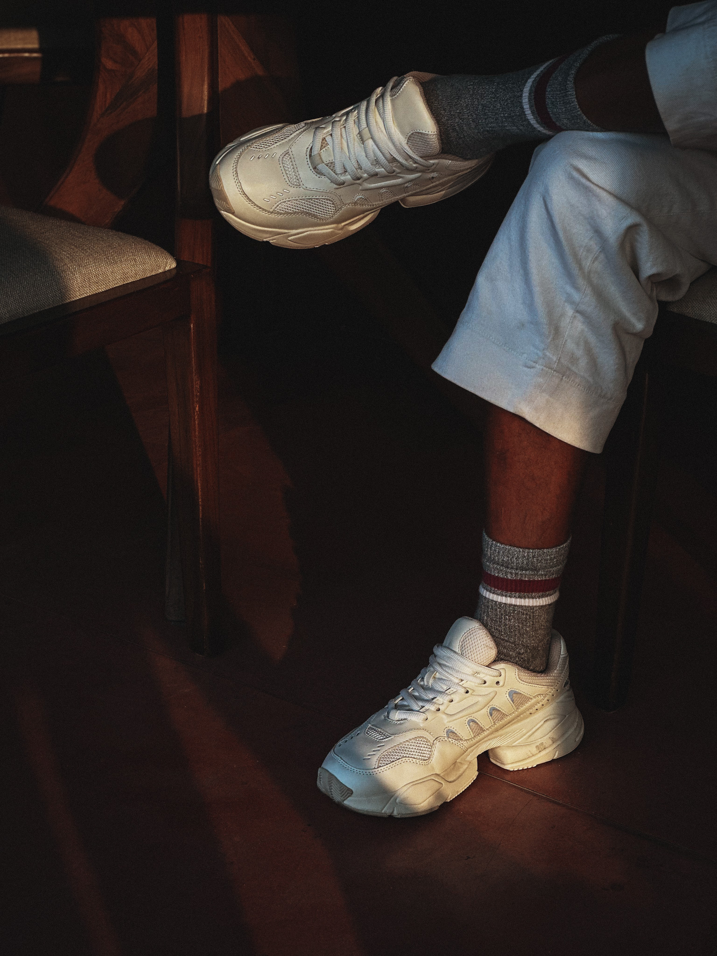 Guest in white sneakers and trousers seated by wooden chair in softly lit interior, illustrating the stylish, relaxed dining experience at Sunday Kitchen, Brazilian restaurant in Bali