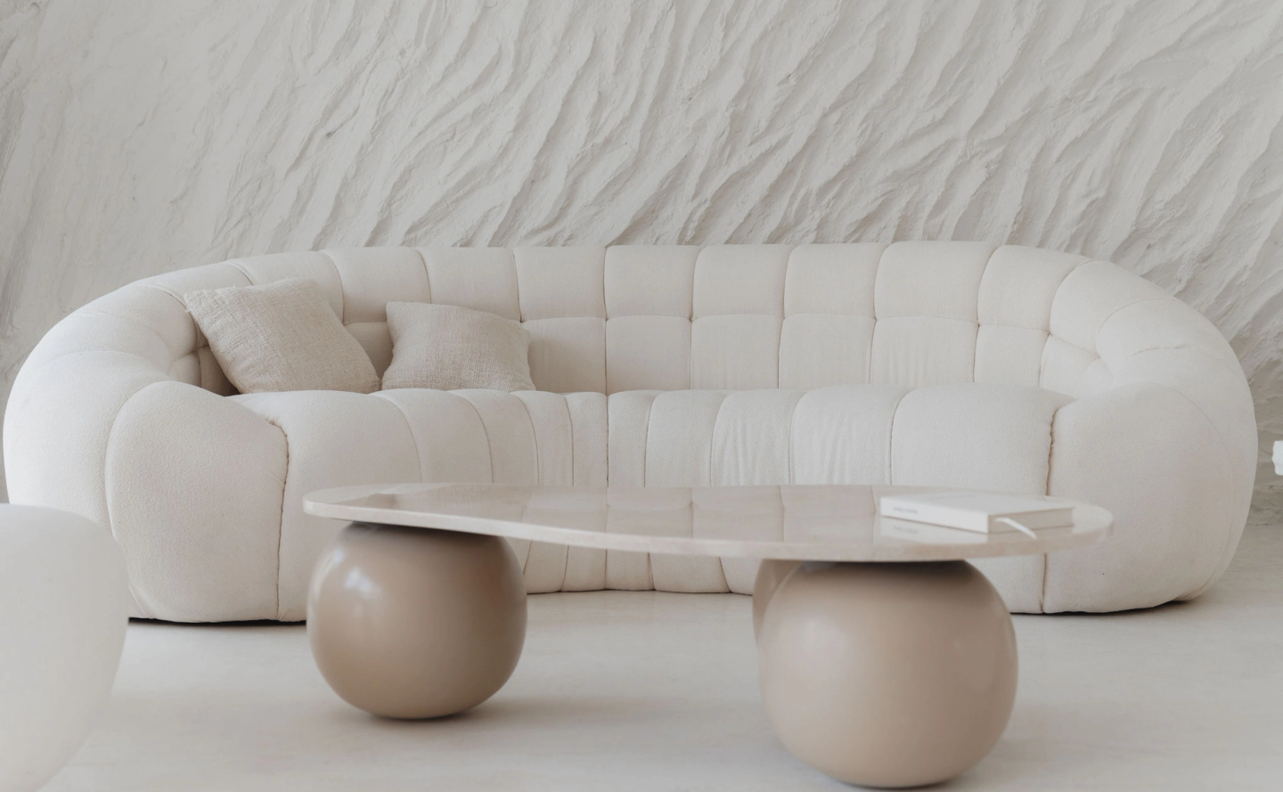 House of Creations Bali – Modern Lounge Sofa and Sculptural Table Modern luxury villa lounge with textured white sofa, neutral pillows, sculptural stone coffee table and accent books at House of Creations Bali