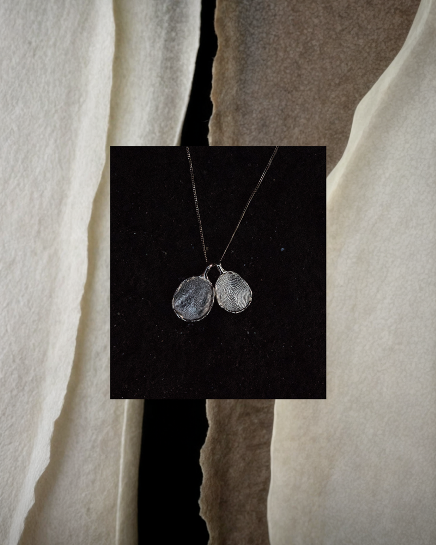 Text: Pair of OMOI Jewelry sterling silver Forever Pendants with fingerprint texture on black backdrop, layered over tactile paper for Shopify website design by Eeze Studio