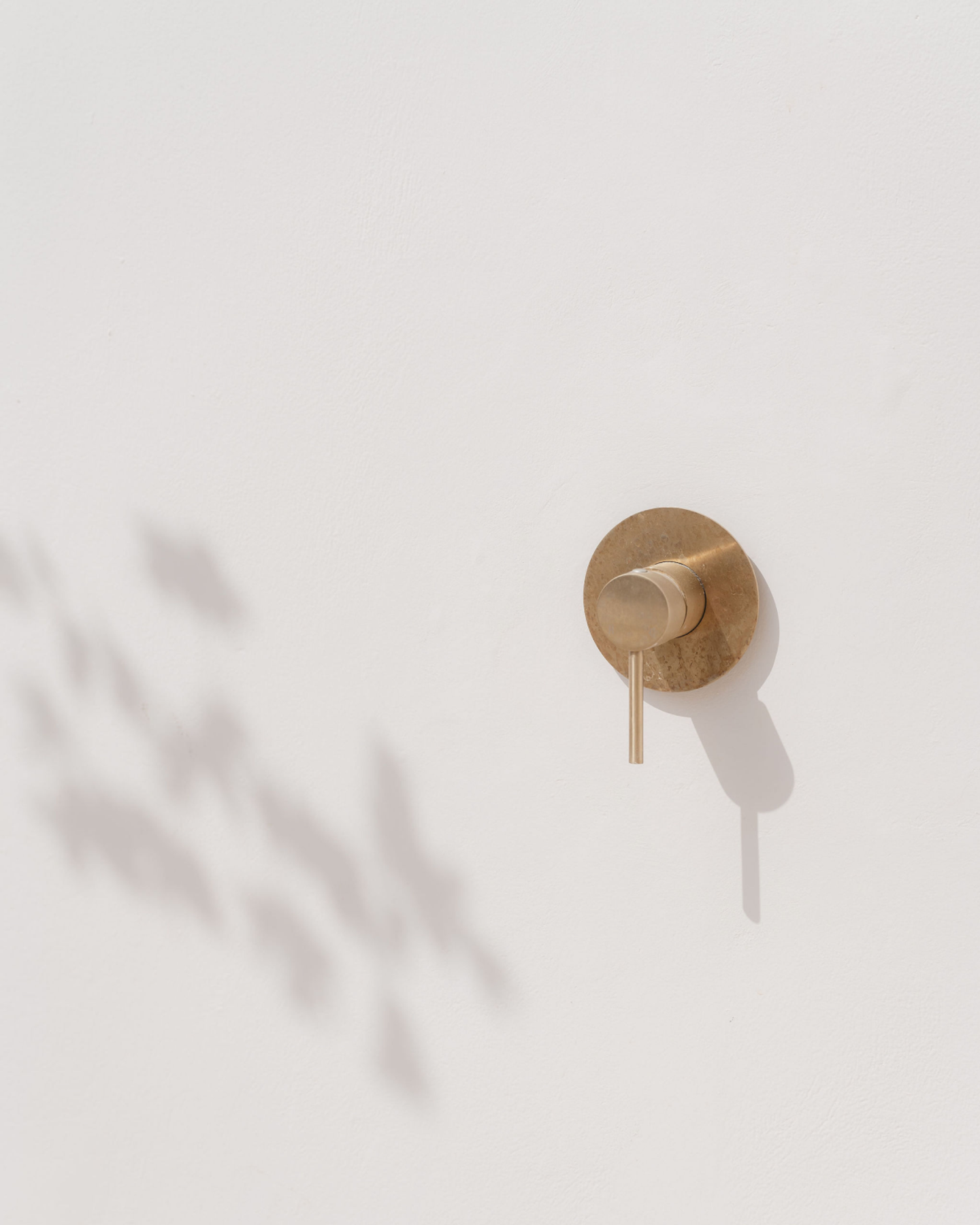 House of Creations Bali – Minimalist Brass Wall Fixture Minimalist brass wall fixture casting a soft shadow on textured white wall, capturing architectural branding and interior design at House of Creations Bali villa