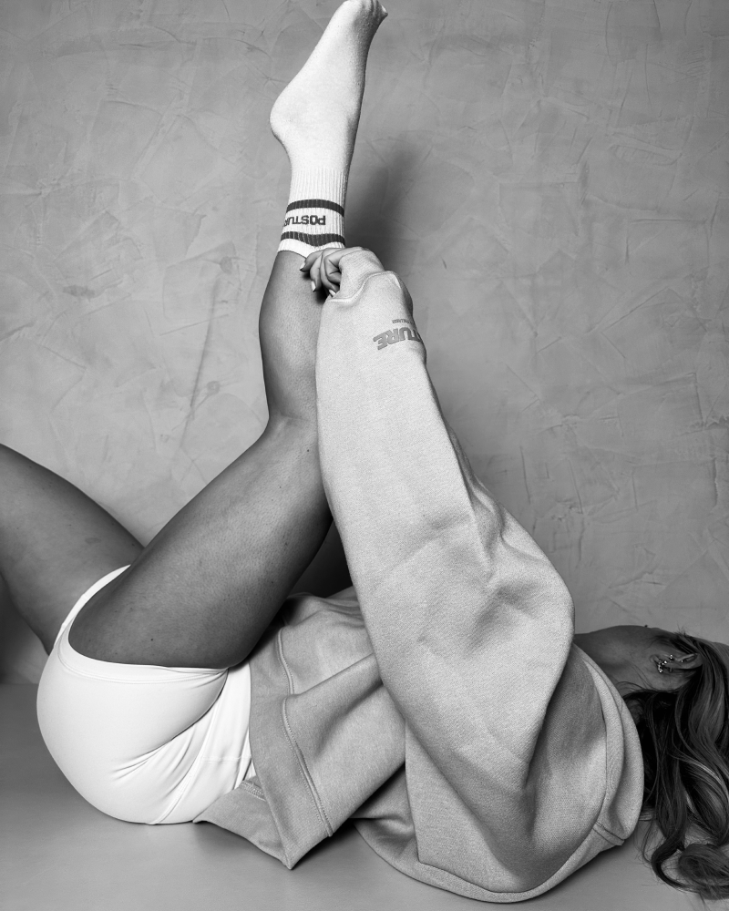 Posture Pilates Monochrome Stretch – Brand Campaign Photography Black and white studio portrait of woman stretching on mat in oversized sweatshirt and branded socks, produced for Posture Pilates rebranding and website design