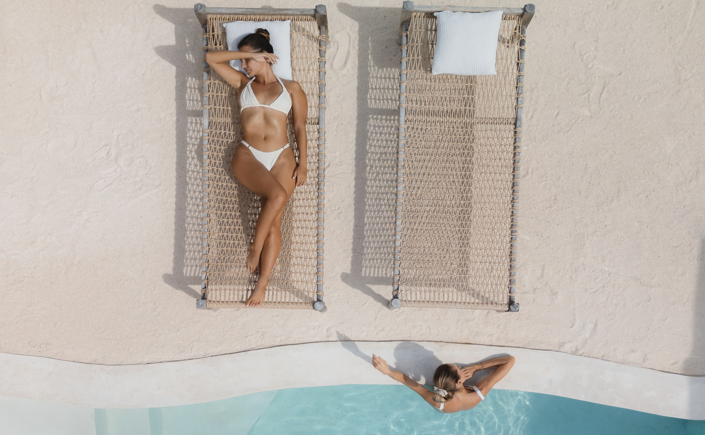 House of Creations Bali – Designer Villa Poolside Lifestyle Photoshoot Aerial view of a woman relaxing on woven sunbed beside turquoise pool, luxury villa designer setting and lifestyle branding for House of Creations Bali