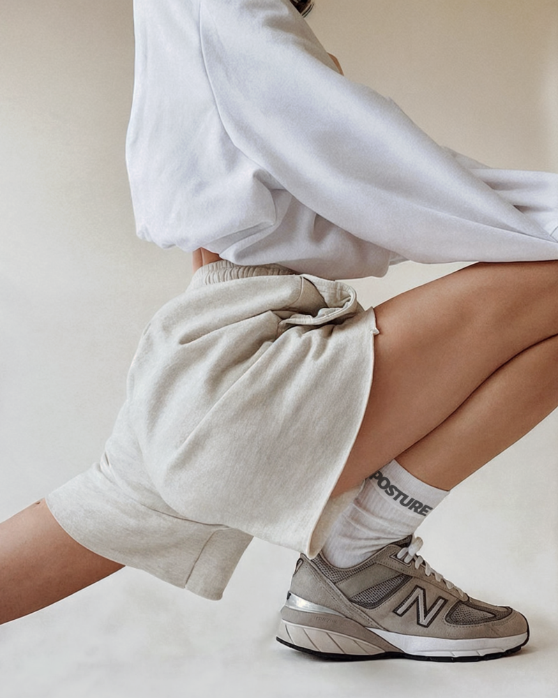 Posture Pilates Lifestyle Shot – Branded Socks and Movement Lifestyle crop of woman stretching in sweatshirt and shorts with Posture branded socks and sneakers, produced for Posture Pilates rebrand and website imagery
