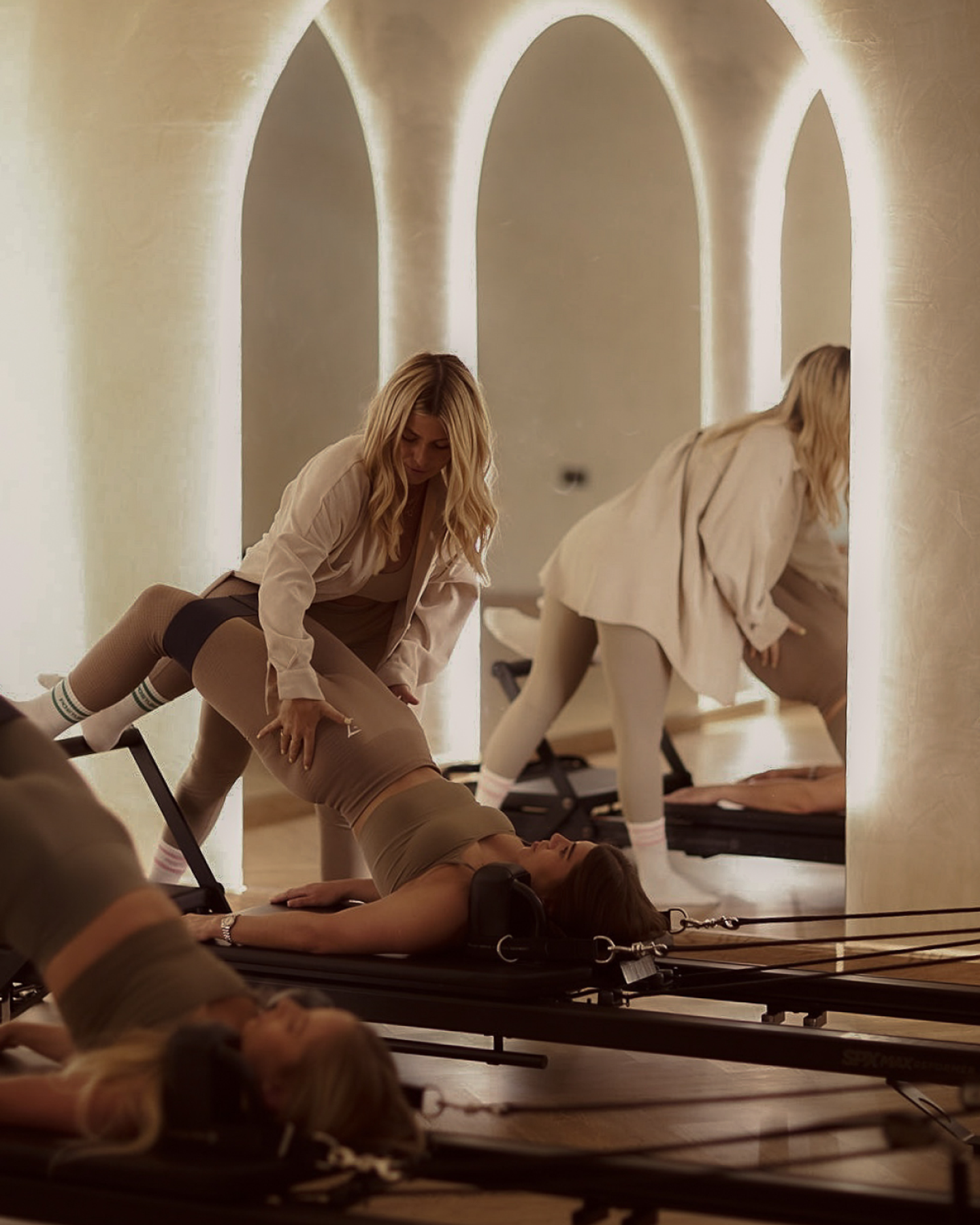 Posture Pilates Class Instruction – Reformer Training in The Palm Dubai Instructor assisting client on reformer in softly lit arched studio, highlighting Posture Pilates coaching and premium class experience in The Palm, Dubai