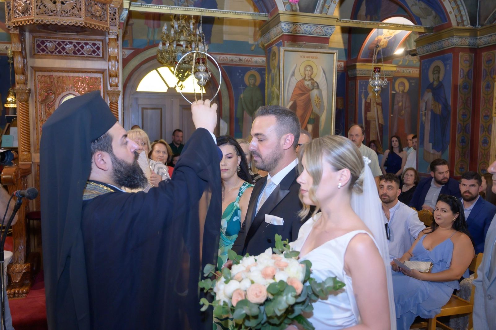 The priest raises the wedding crowns over the bride and groom inside a church with painted icons.