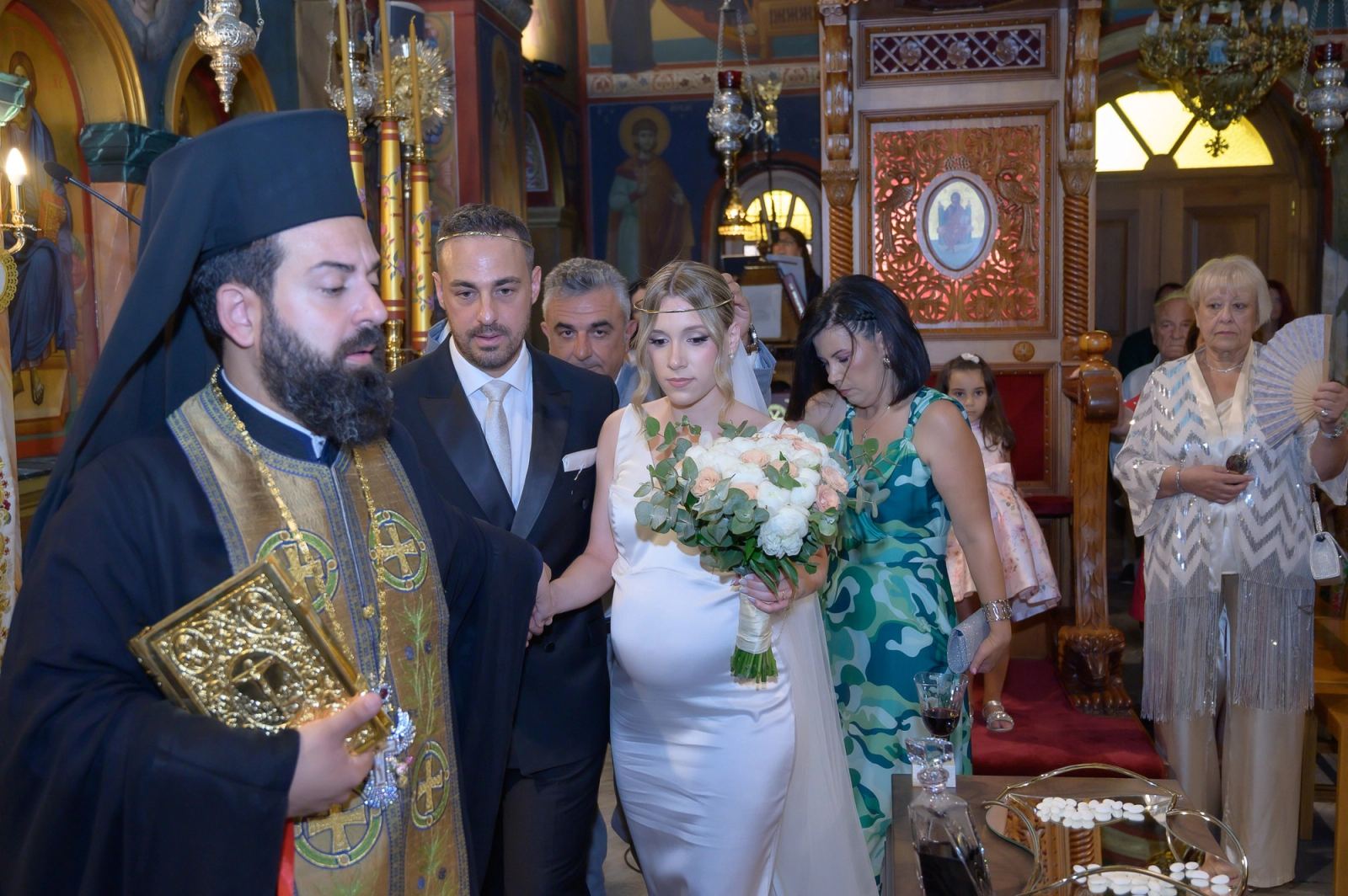 The priest holding the Gospel leads the bride and groom around the ceremony table.
