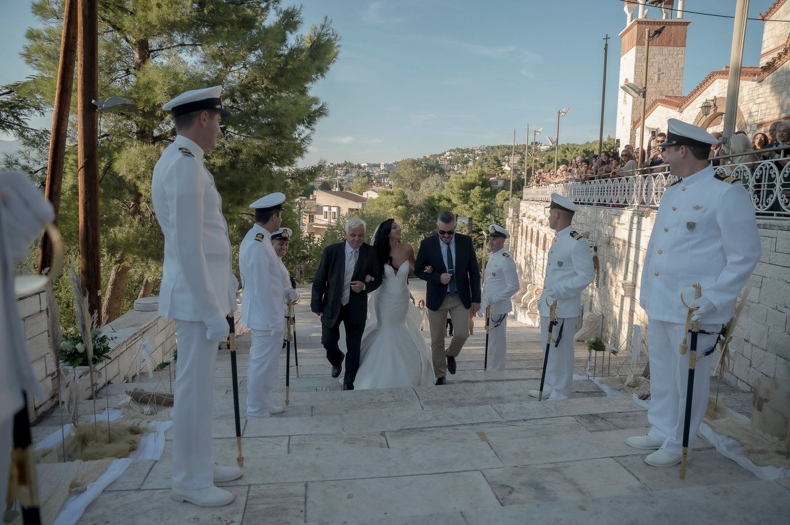 Η νύφη ανεβαίνει πέτρινα σκαλιά προς εκκλησία ανάμεσα σε αξιωματικούς με λευκές στολές και ξίφη.