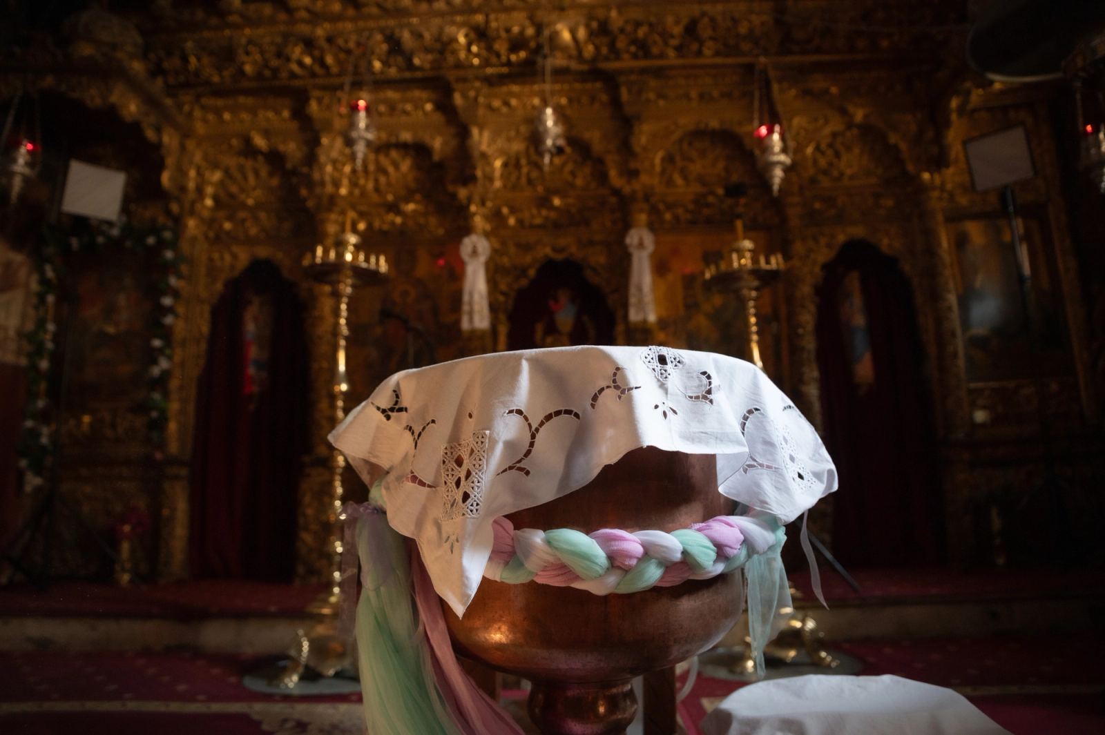 The font with an embroidered cover and a colorful braid in front of a gilded carved iconostasis.