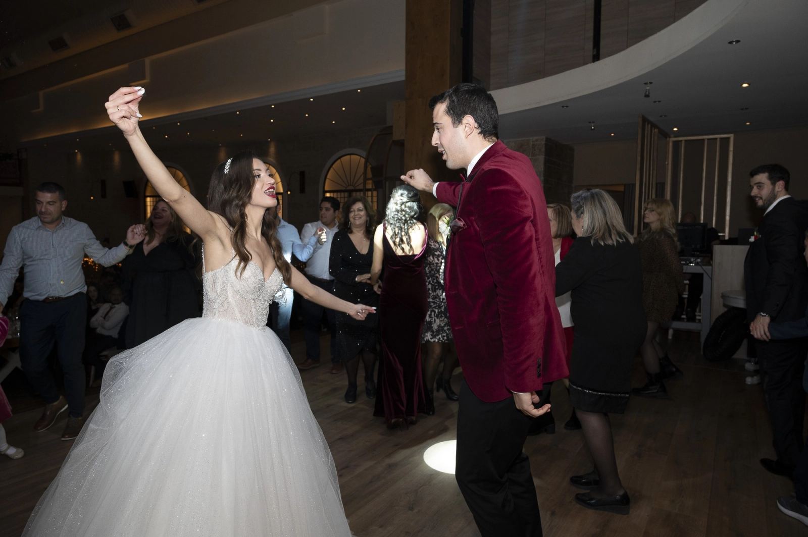 The bride dances with one arm raised, facing the groom, as guests fill the dance floor.