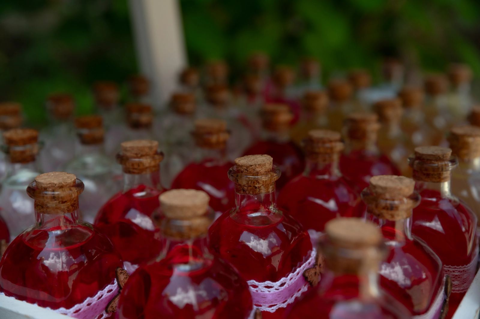 Rows of small glass bottles with red liquid, cork stoppers and lace trim.