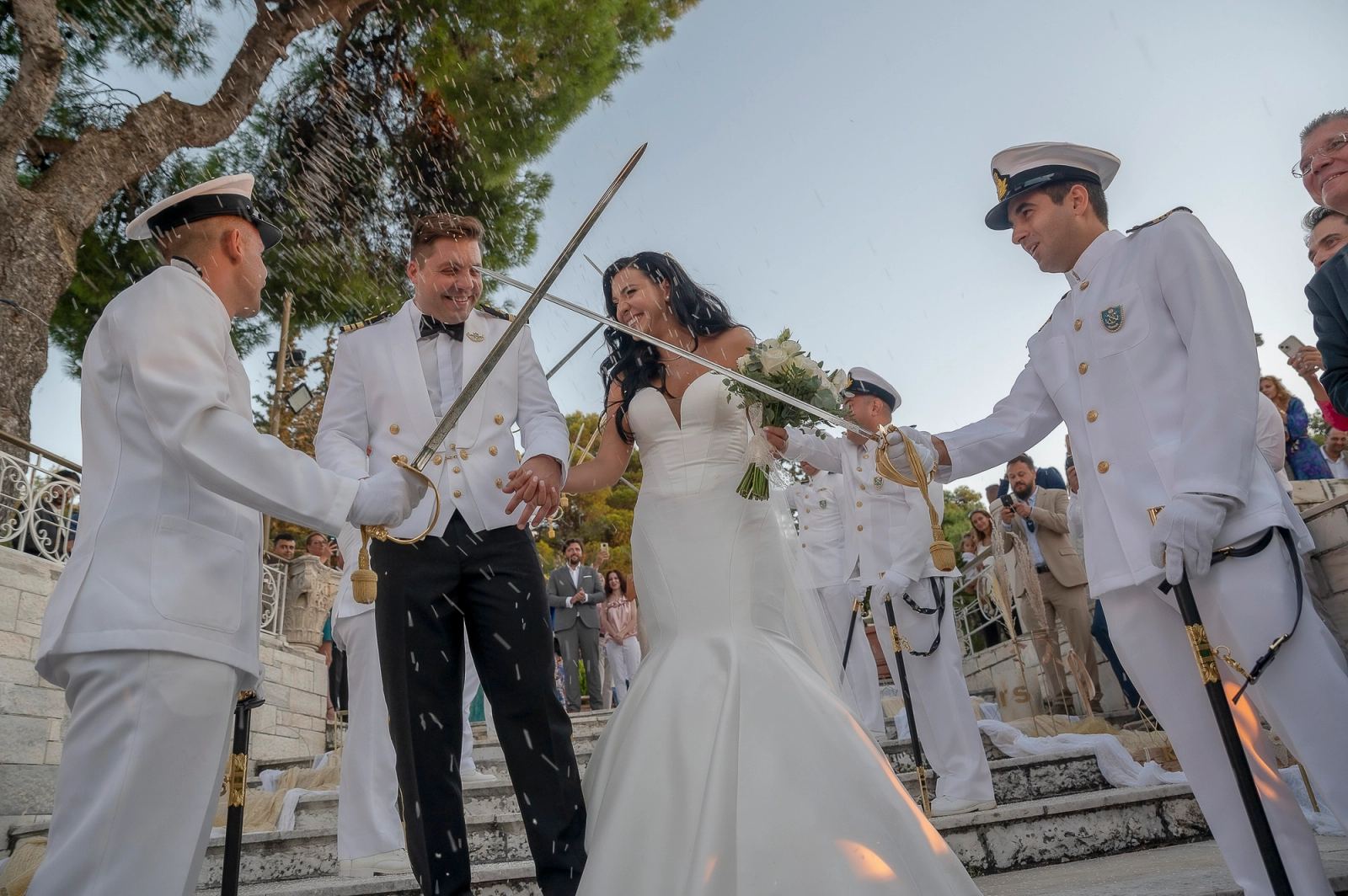 Ναυτικοί με λευκές στολές κρατούν σπαθιά πάνω από τη νύφη και τον γαμπρό ενώ πέφτει ρύζι.