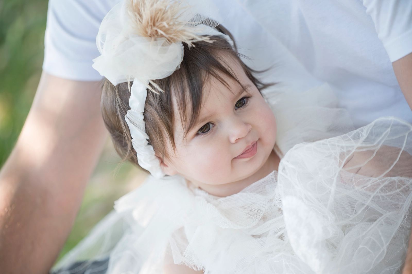 Close-up of the baby wearing a white feathered headband and a tulle dress.