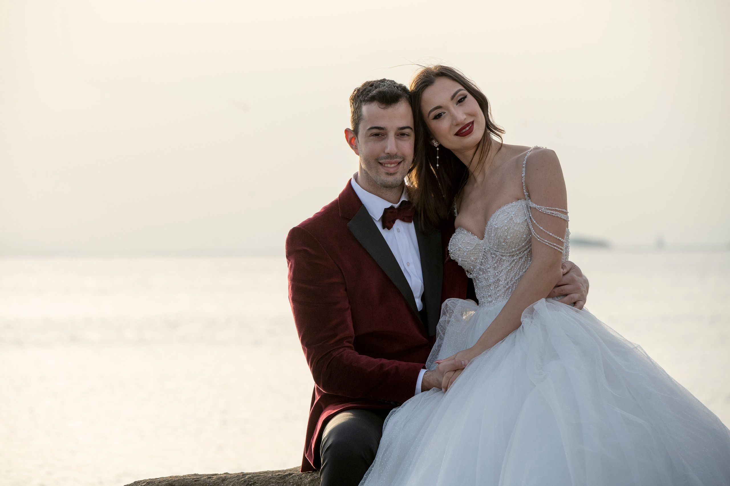 Bride and groom sitting on a rock by the sea