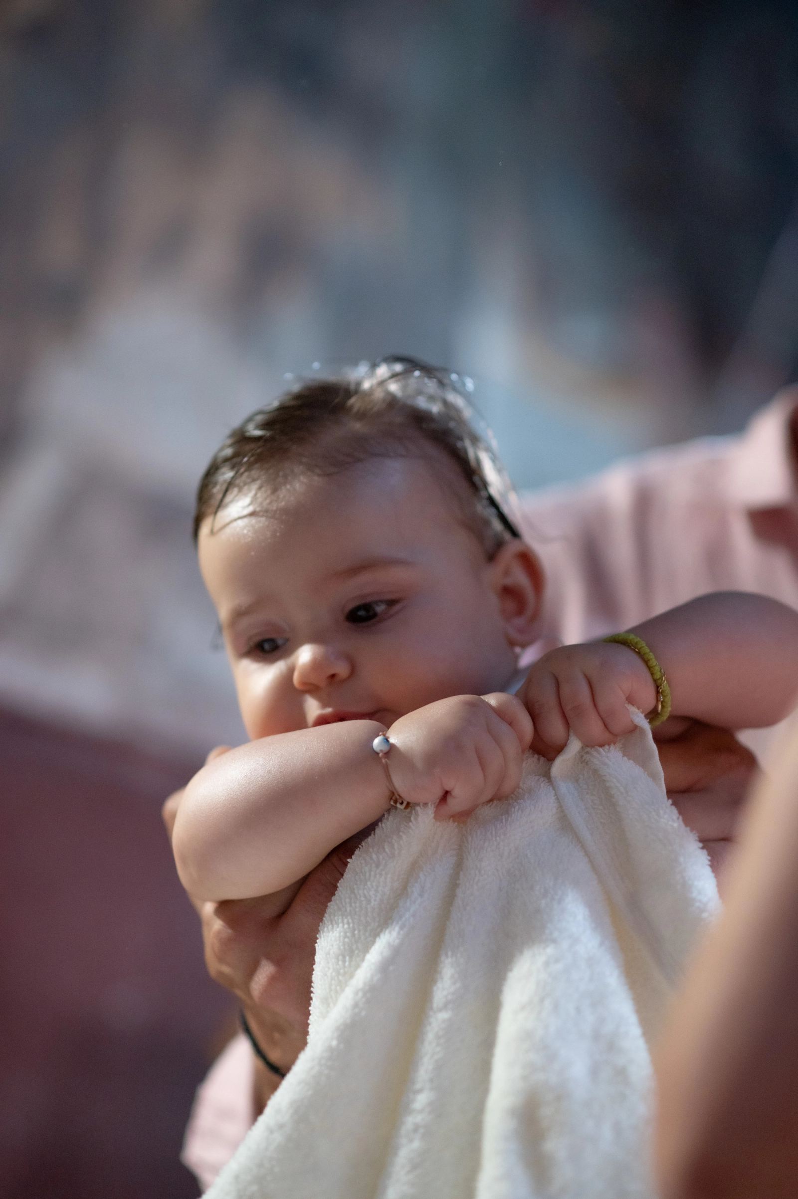 The baby with wet hair holds a white towel after the baptism.