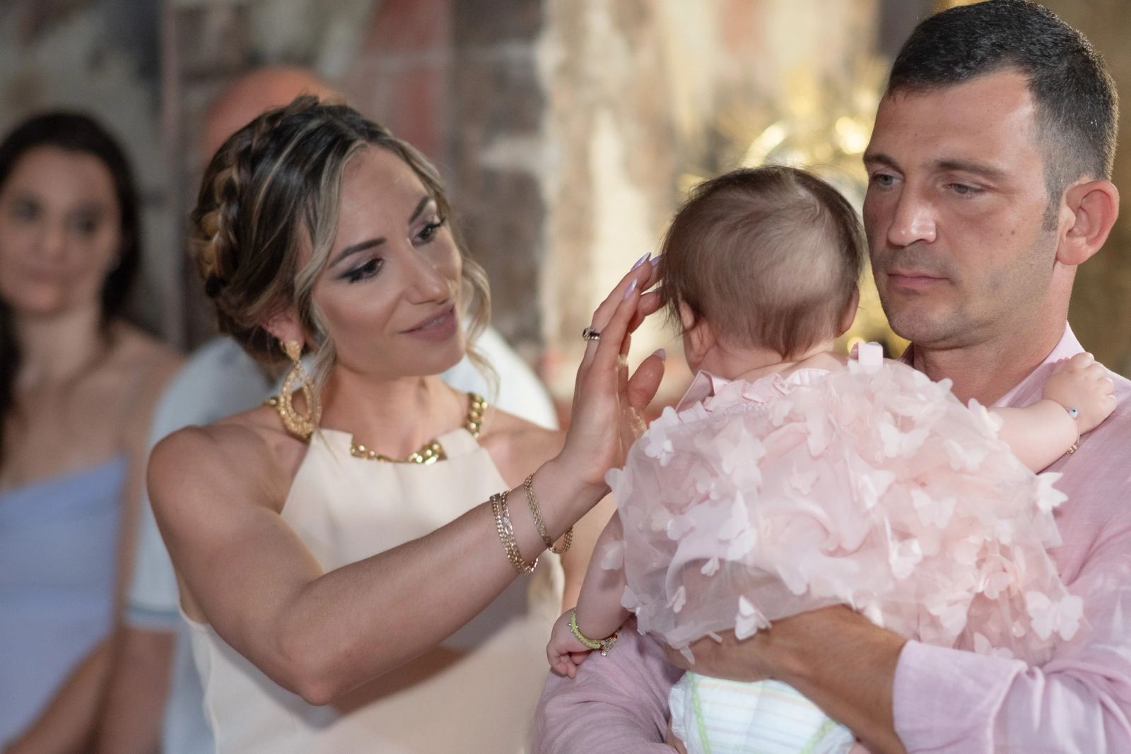A woman touches the head of the baby held by a man in a pink shirt inside the church.