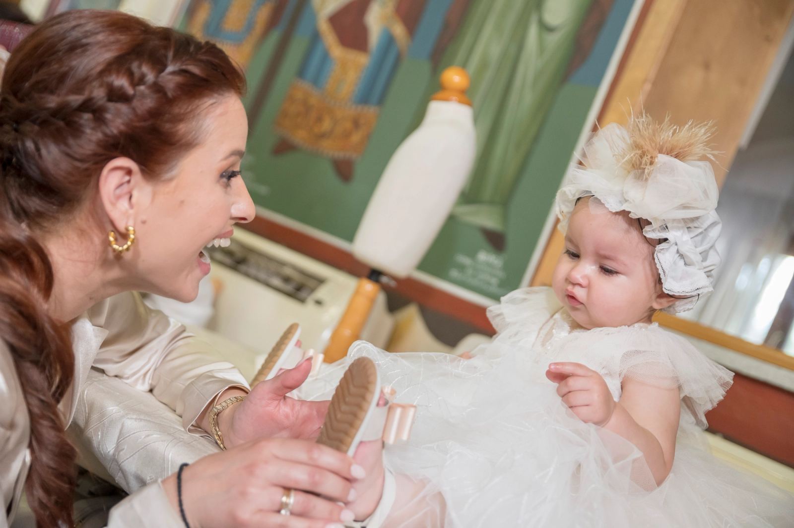 A woman puts sandals on the baby in a white tulle dress and hair bow.
