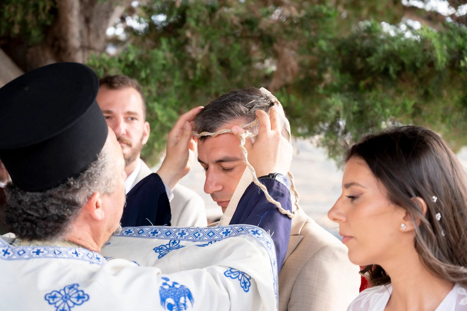 Ο ιερέας τοποθετεί στέφανο από σχοινί στο κεφάλι του γαμπρού, με τη νύφη δίπλα.