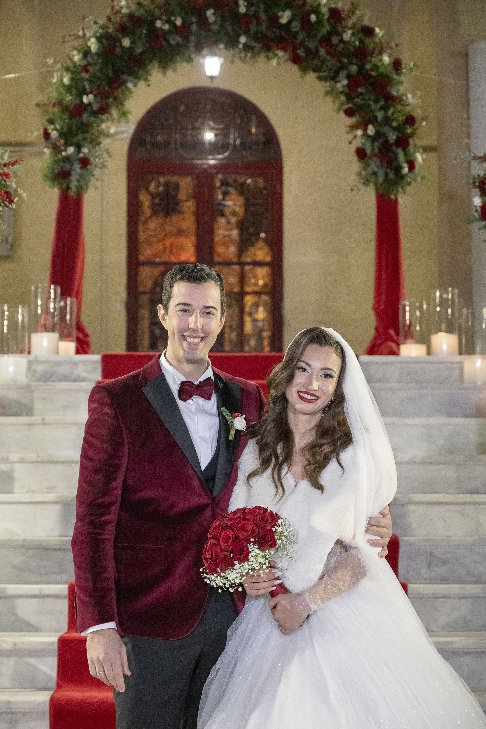 The bride and groom on the steps of Agios Christoforos beneath a floral arch