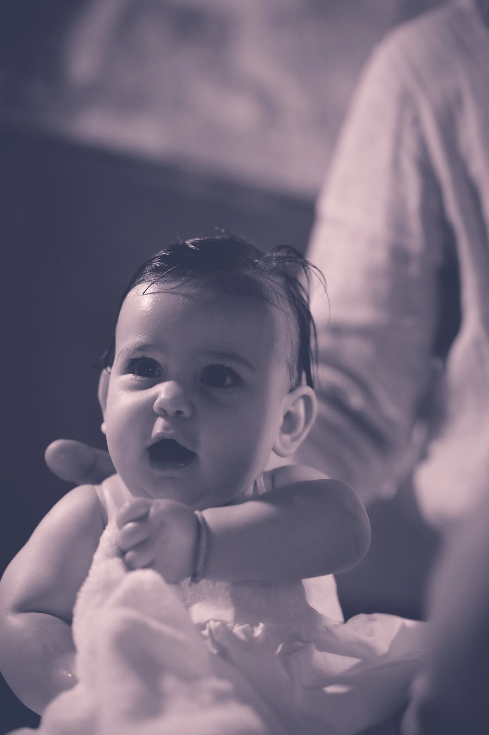 The baby with wet hair looks up, in a monochrome photo with a purple tone.