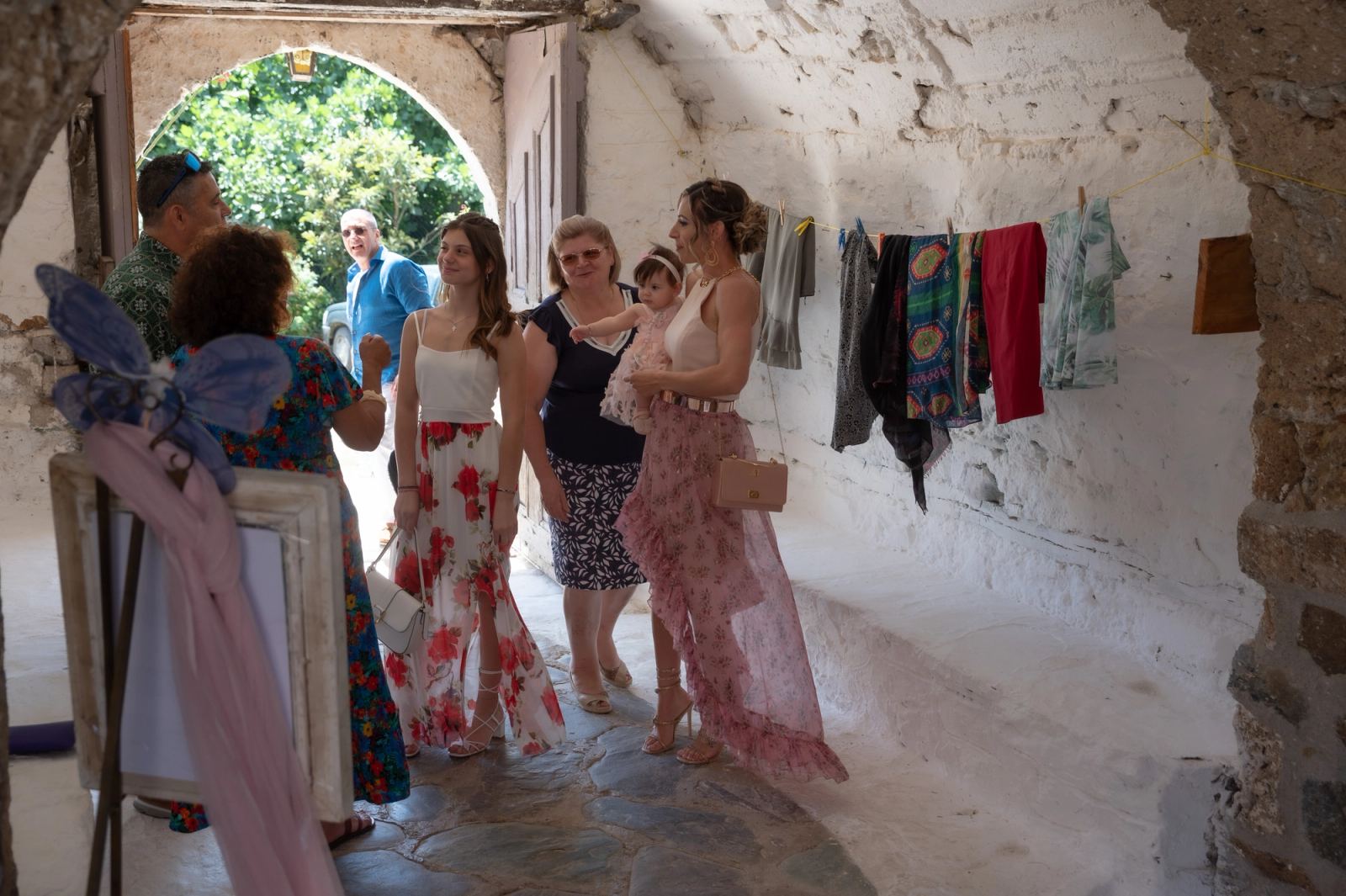 Guests and a woman holding the baby in a whitewashed passage with hanging woven textiles.