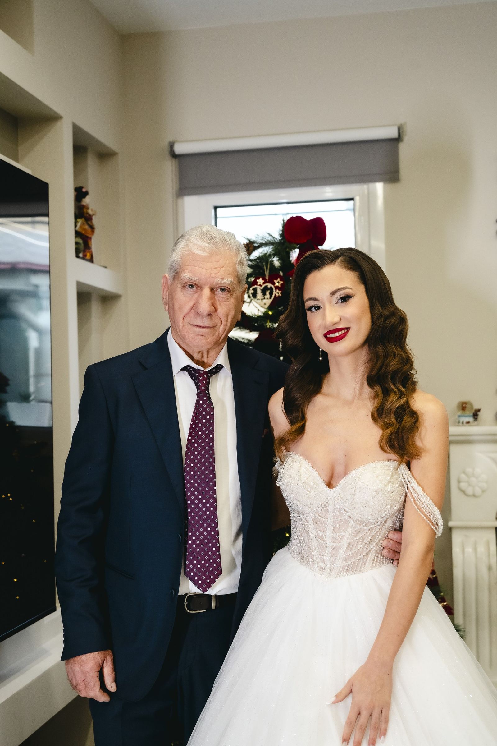 The bride in her gown poses with an older man in a suit in a living room