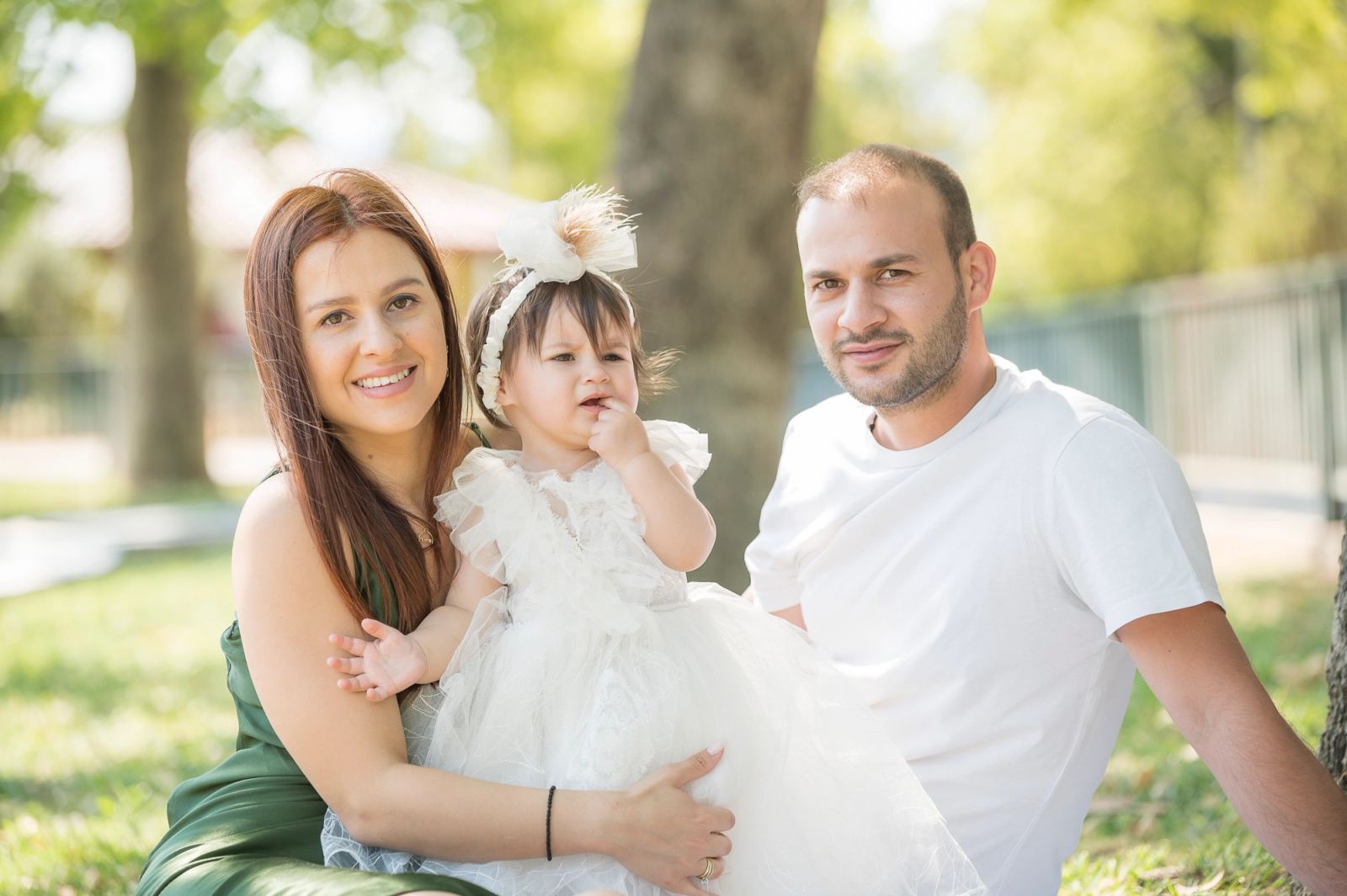 A woman in a green dress and a man in a white T-shirt sit with the baby in a park.