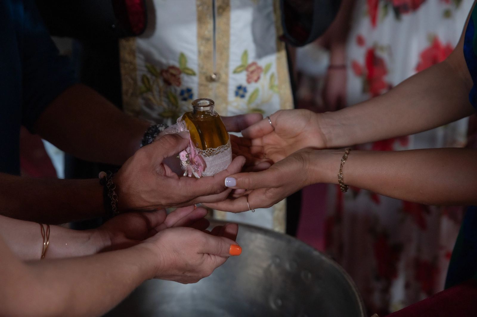 Hands hold a bottle of oil with a pink ribbon above a metal font.