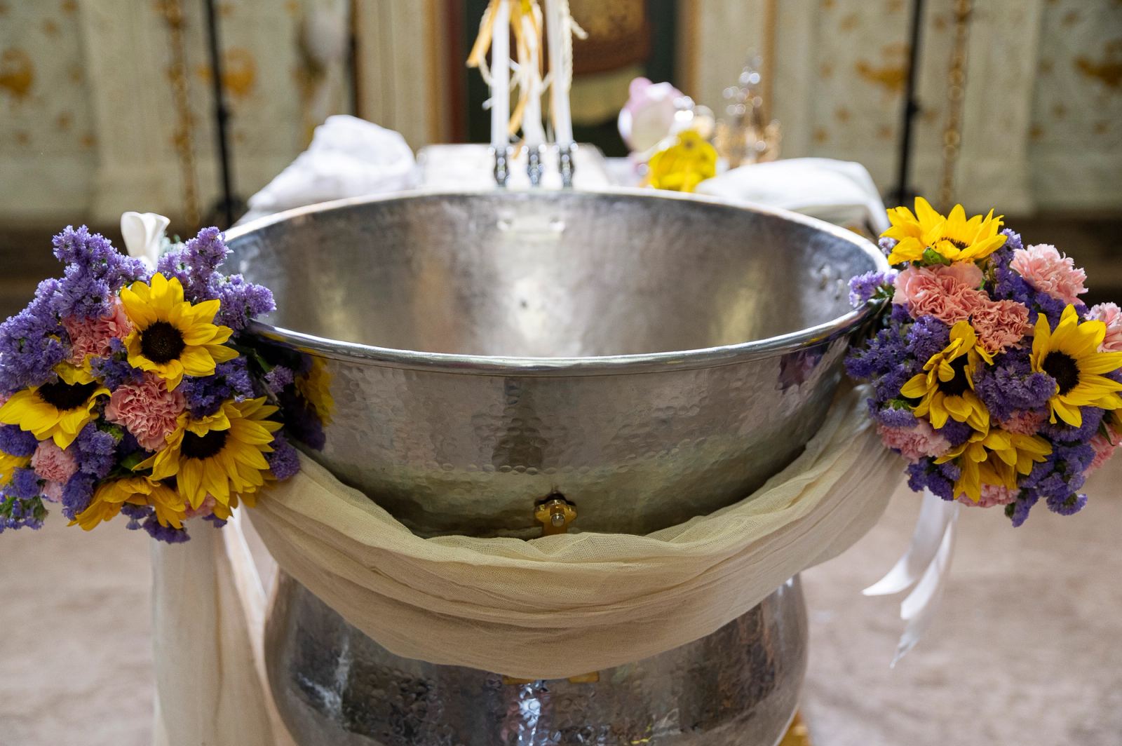 Silver baptismal font decorated with sunflowers, carnations and purple flowers inside a church.