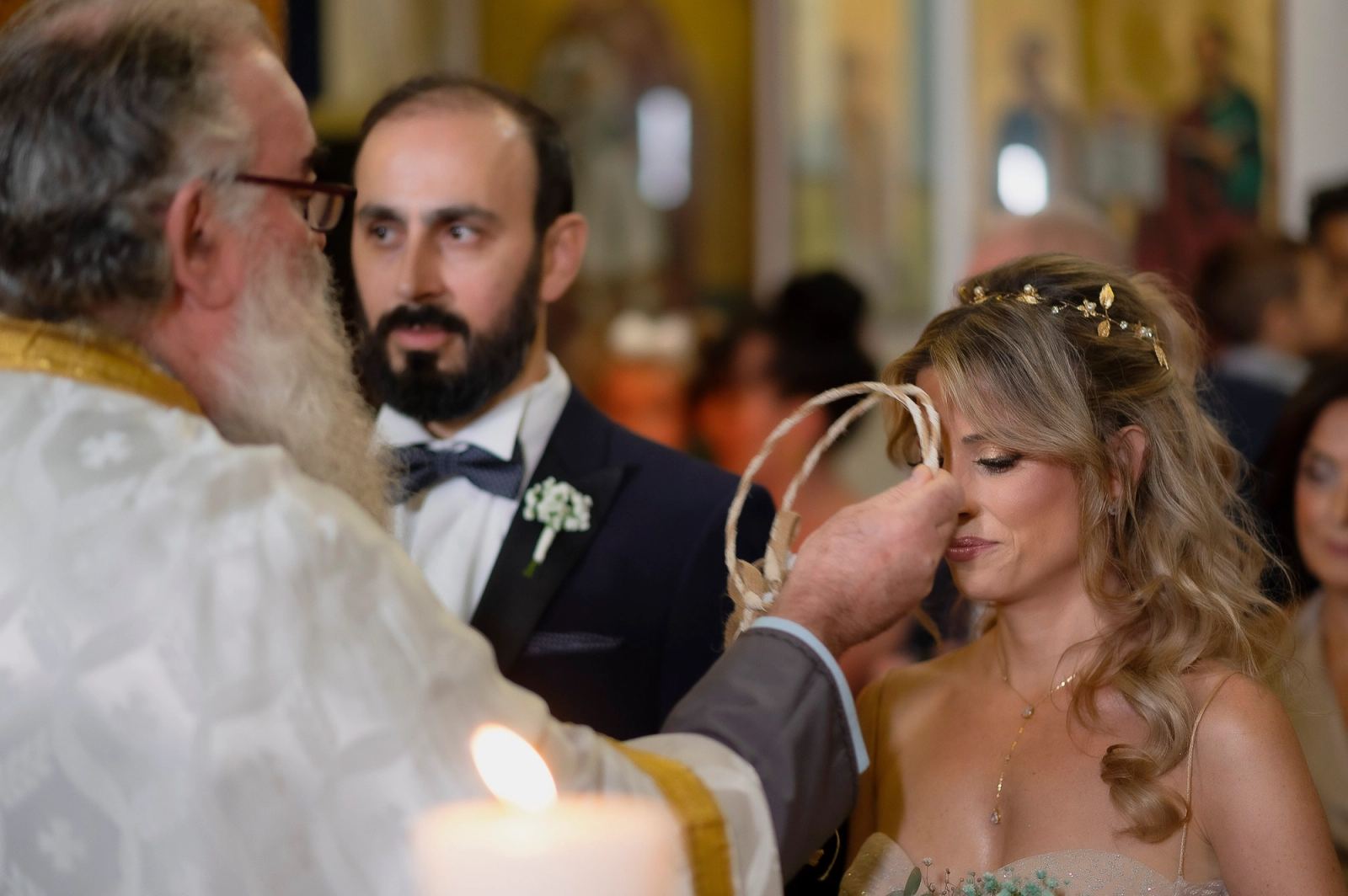 Ο ιερέας φέρνει τα στέφανα στο πρόσωπο της νύφης, με τον γαμπρό δίπλα και αναμμένο κερί μπροστά.