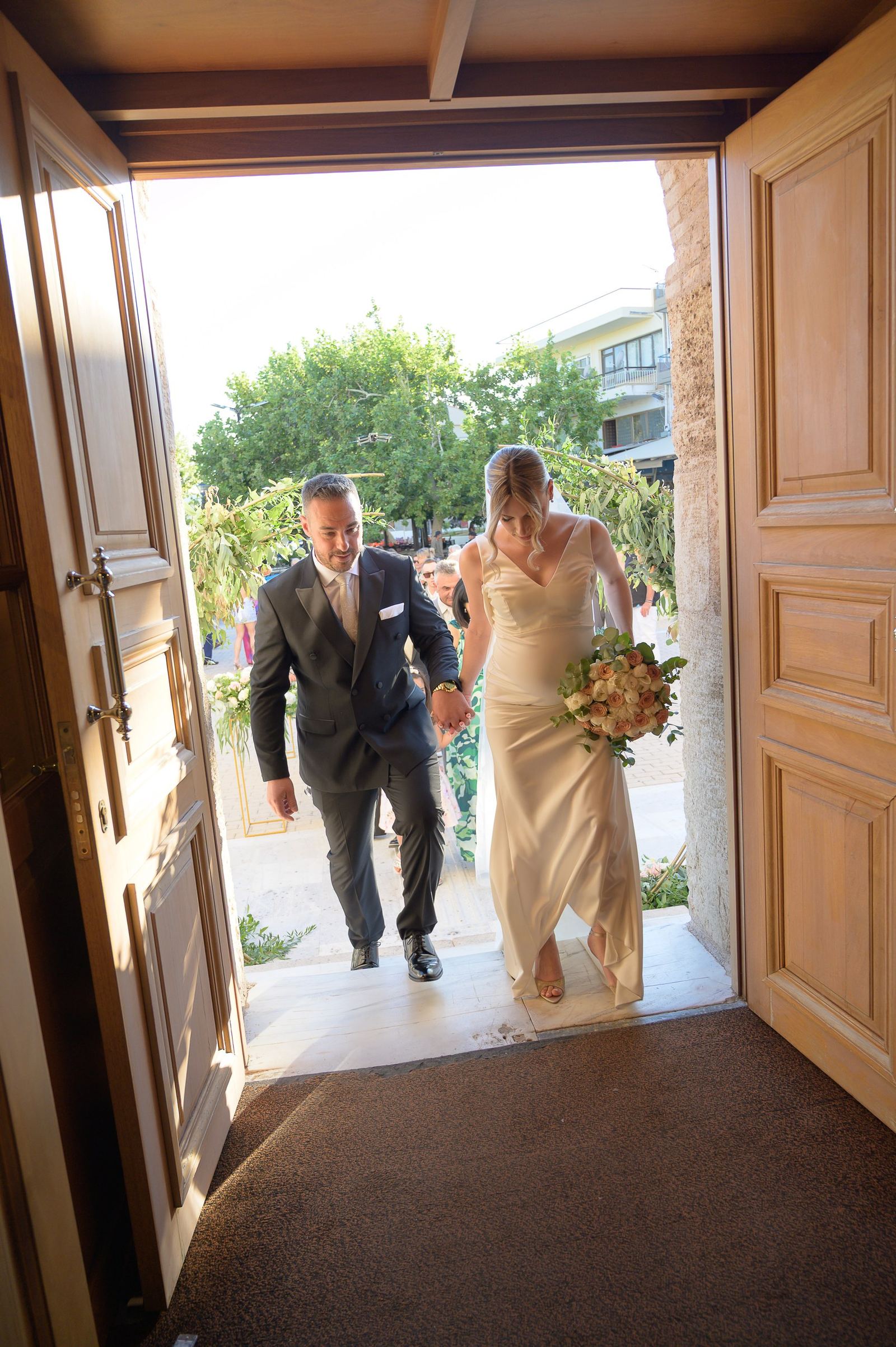 The bride and groom walk hand in hand through the wooden door of the Church of the Analipsi.